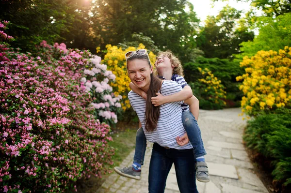 De jonge vrouw houdt de jongen op de schouders — Stockfoto