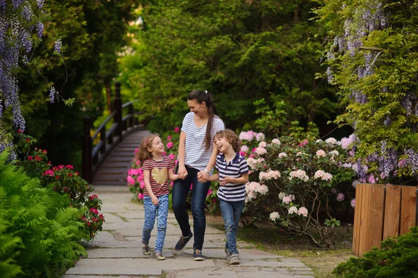 Jonge vrouw lopen met de kinderen in de weelderige tuin. — Stockfoto