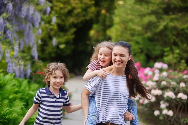 Молодая женщина с двумя детьми, гуляющая в летнем саду — стоковое фото