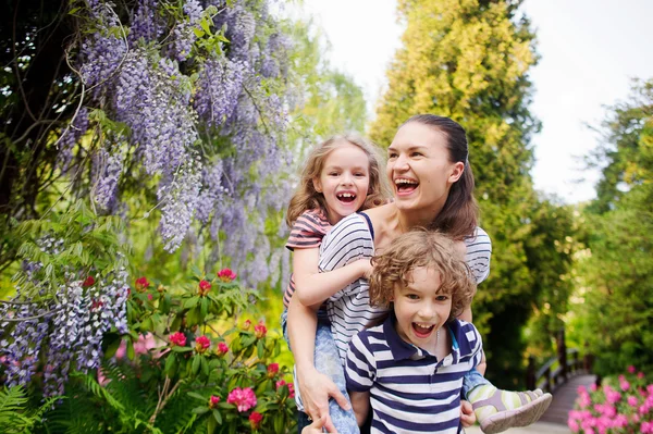 Jonge vrouw met haar dochter en zoon op de achtergrond van een bloeiende tuin — Stockfoto