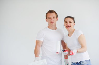 Silindirleri boyalı adam ve kız beyaz bir duvara karşı duruyorlar..