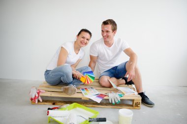 Adam ve kız boş odada ahşap palet üzerinde oturup, bir dekor renk seçin.