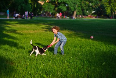 Çocuk neşeyle yaz aylarında parkta köpek ile oynar.
