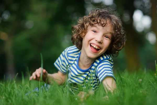 Мальчик 8-9 лет лежит в зеленой траве и смеется. . — стоковое фото