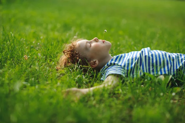 El muchacho de 8-9 años yace sobre la espalda en la hierba espesa verde . —  Fotos de Stock