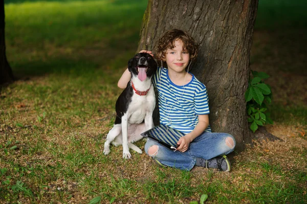 Jongen met hond zit op de aarde onder een boom. — Stockfoto