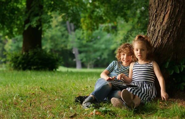 男孩和7-8岁的女孩坐在公园里的一棵大树下. — 图库照片