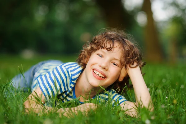 Мальчик лежит на зеленой лужайке в парке, протянув руку . — стоковое фото