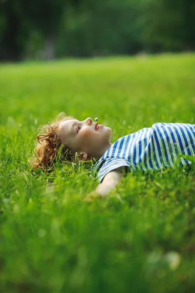 De kleine jongen ligt op een groen gazon in Park. — Stockfoto