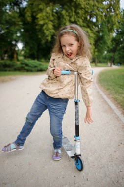 Eğilerek scooter bir tekerlek üzerinde durmak için küçük kız.