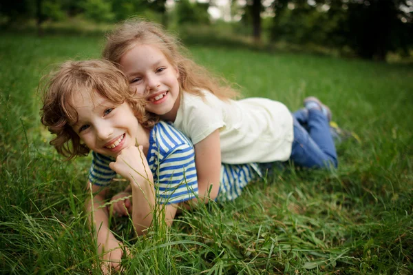 Duas crianças mentem em uma grama verde . — Fotografia de Stock