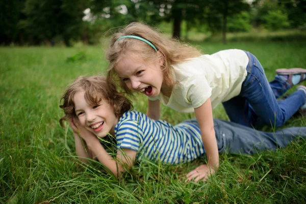 Twee kinderen zijn ondeugend op een groen gras. — Stockfoto