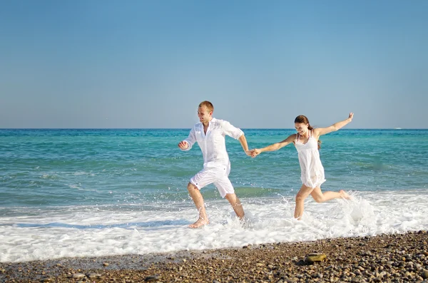 Feliz joven pareja corre habiendo unido las manos en la costa del mar . — Foto de Stock