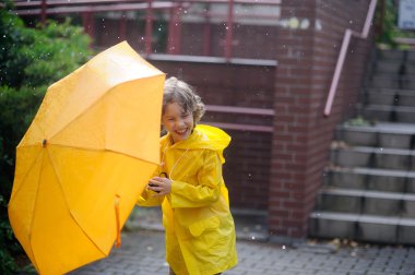 Boy 8-9 years walk with a yellow umbrella in the yard during rain.