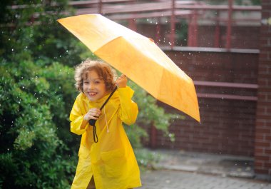 Yağmur altında durmak için parlak sarı yağmurluk çocukta.