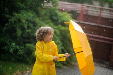Parlak sarı yağmurluk çocukta bir şemsiye ayakta bir yağmur altında açılır.