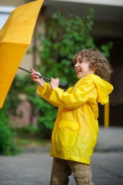 Delikanlı bir şemsiye windflaws üzerinden tutmak 8-9 yıl parlak sarı yağmurluk içinde çalışır.