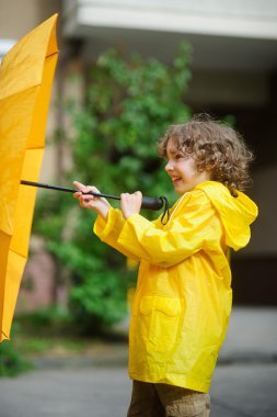 Sarı yağmurluk çocuk elinde bir şemsiye ile.