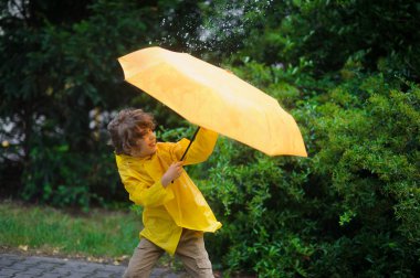 Çocuk 8-9 yıl parlak sarı yağmurluk içinde rüzgar kusurları üzerinden bir Şemsiyeyi tut dener.
