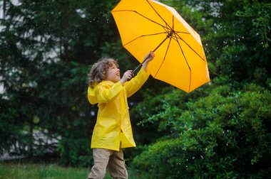 Küçük çocuk bir parlak sarı şemsiye ve yağmurluk sıcak yaz yağmur altında.