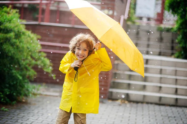Little fellow in bright yellow raincoat is at the yard under a pouring rain. — Stock Photo, Image
