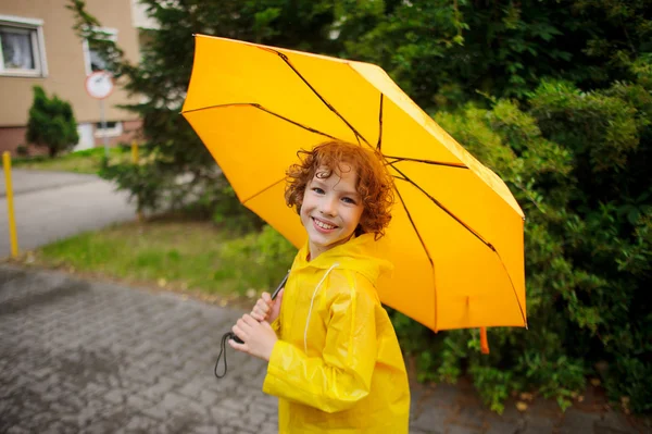 Cheerful boy of 8-9 years under a yellow umbrella. — Stock Photo, Image