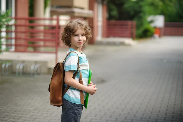 Colegial va a la escuela con una mochila detrás de los hombros . — Foto de Stock