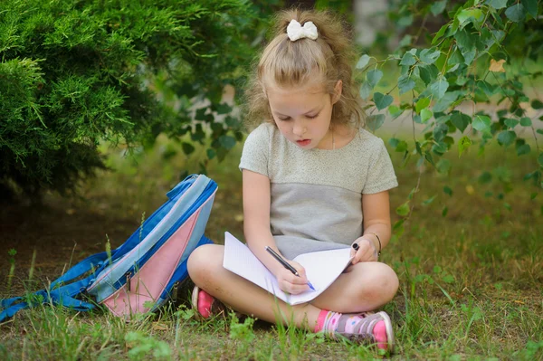 Écolière de l'école primaire se trouve ayant croisé les jambes sous un arbre et fait des devoirs . — Photo