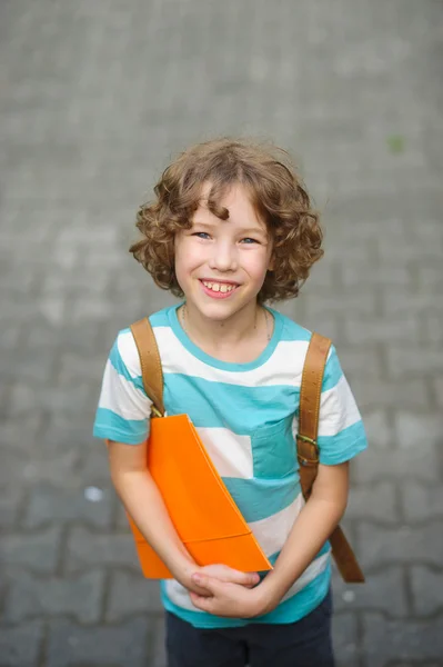 De Fair haired krullend school jongen kijkt in de camera en glimlacht. — Stockfoto