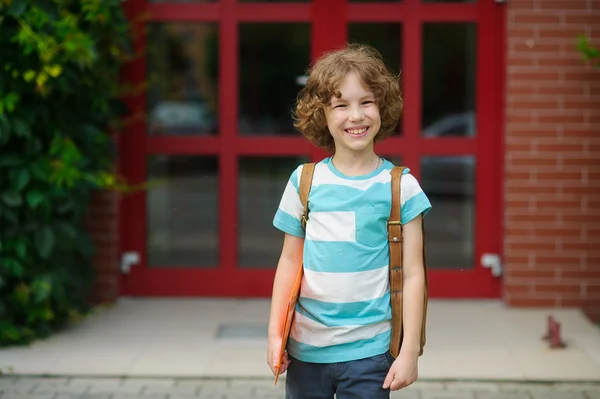 De kleine school jongen staat op een schoolplein en lacht vrolijk. — Stockfoto