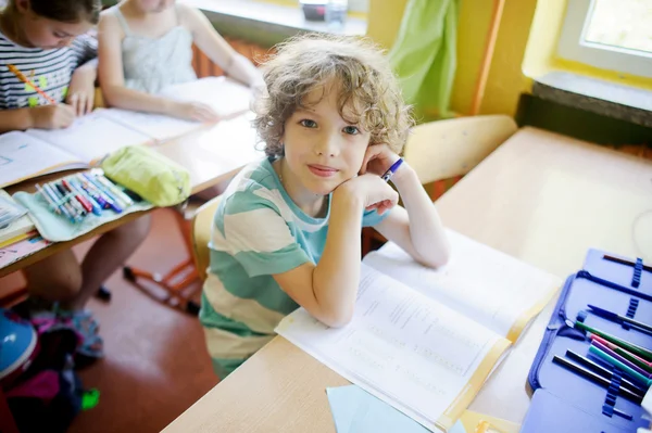 L'écolier bouclé aux cheveux blonds est assis à un bureau d'école en classe — Photo