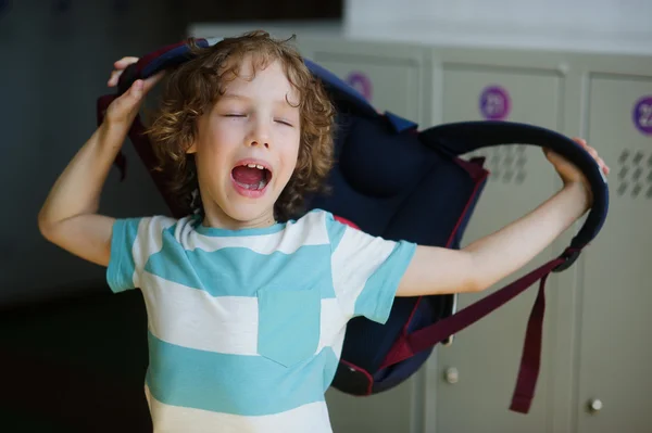 Tired little student standing in the hall near the lockers and wears a backpack. — Stock Photo, Image