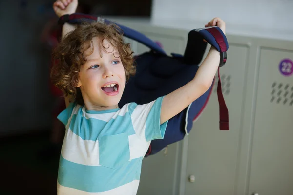 Tired little student standing in the hall near the lockers and wears a backpack. — Stock Photo, Image