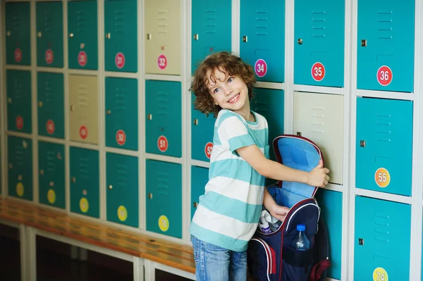Malý školák, stojící v hale poblíž skříňky. — Stock fotografie