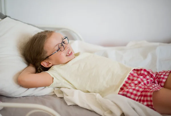 Забавная маленькая девочка в очках, лежащая в его постели . — стоковое фото