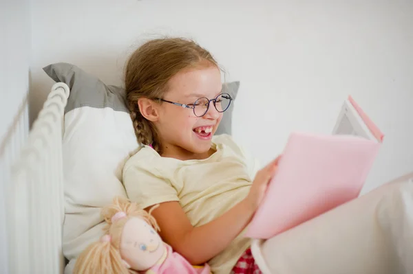 Chica divertida con gafas leyendo un libro mientras está acostado en la cama . —  Fotos de Stock