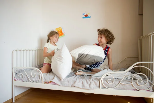 Fratellino e sorella in scena una lotta cuscino in camera da letto . — Foto Stock