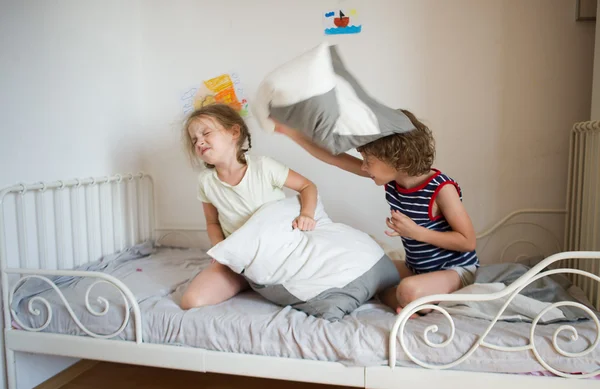 Kleine jongen en meisje geënsceneerd een kussengevecht op het bed in de slaapkamer. — Stockfoto