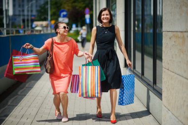İki genç kadın elinde satın almalarla sokakta yürüme.