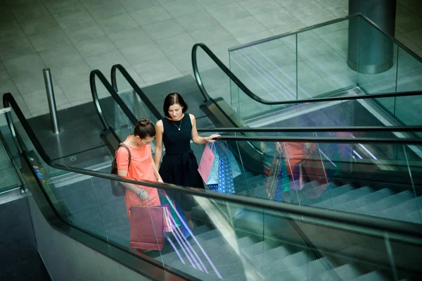 Dwóch zmęczonych młodych kobiet klientów na schody ruchome w centrum handlowym. — Zdjęcie stockowe