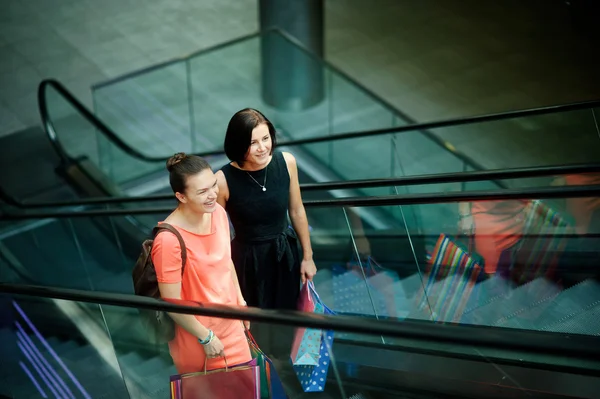 Dwie młode koleżanki na schodach ruchomych w centrum handlowym. — Zdjęcie stockowe