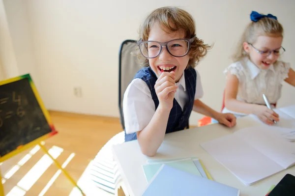 Lächerliche kleine Studenten mit Brille, Junge und Mädchen, teilen sich den gleichen Schreibtisch. — Stockfoto