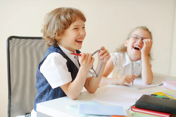 Lustige kleine Schulkinder, Junge und Mädchen, sitzen an einem Schreibtisch. — Stockfoto