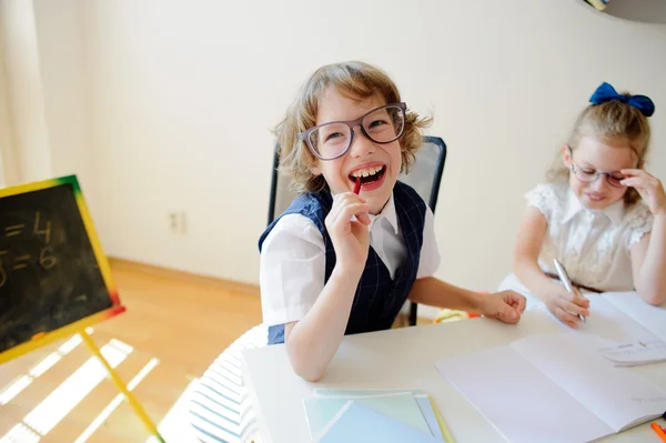 Lustige kleine Schulkinder mit Brille, Junge und Mädchen, sitzen an einem Schreibtisch. — Stockfoto