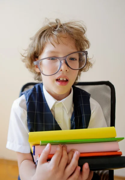 Der zerzauste kleine Schuljunge hält einen Stapel Schulbücher in der Hand und lächelt. — Stockfoto