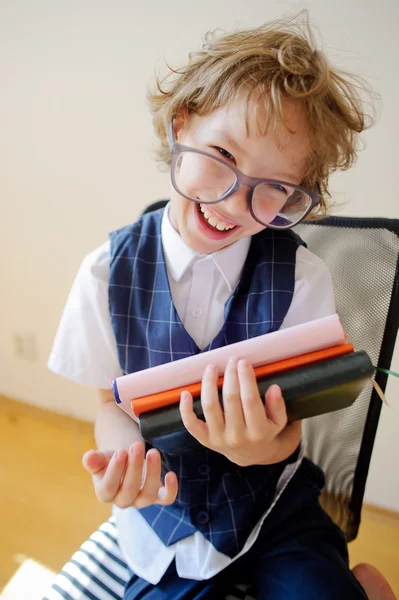 Der zerzauste kleine Schuljunge hält einen Stapel Schulbücher in der Hand und lächelt. — Stockfoto