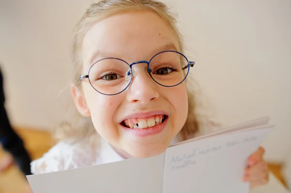 Nettes kleines Schulmädchen mit Brille zeigt ihr Copybook. — Stockfoto