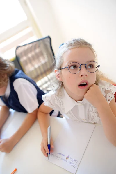 Liten skolflicka i en grundskola sitter vid ett skrivbord i omtanke. — Stockfoto