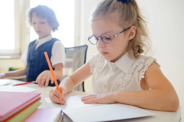 Nettes kleines Schulmädchen mit Brille schreibt fleißig in ein Werbebuch. — Stockfoto