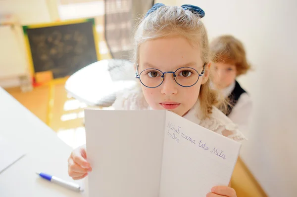 Nettes kleines Schulmädchen mit Brille zeigt ihr Copybook. — Stockfoto